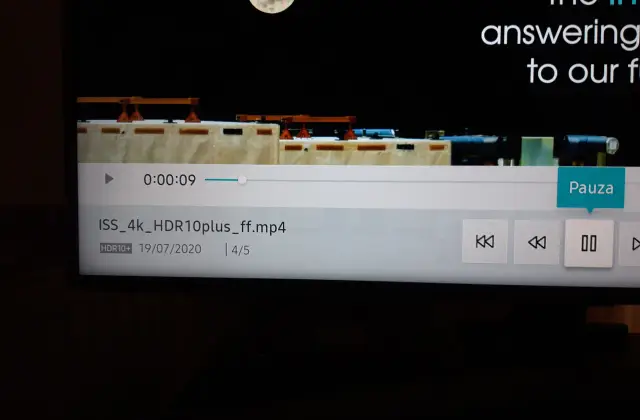 Ekran telewizora z interfejsem odtwarzacza wideo, widoczny fragment filmu z ISS i księżycem.